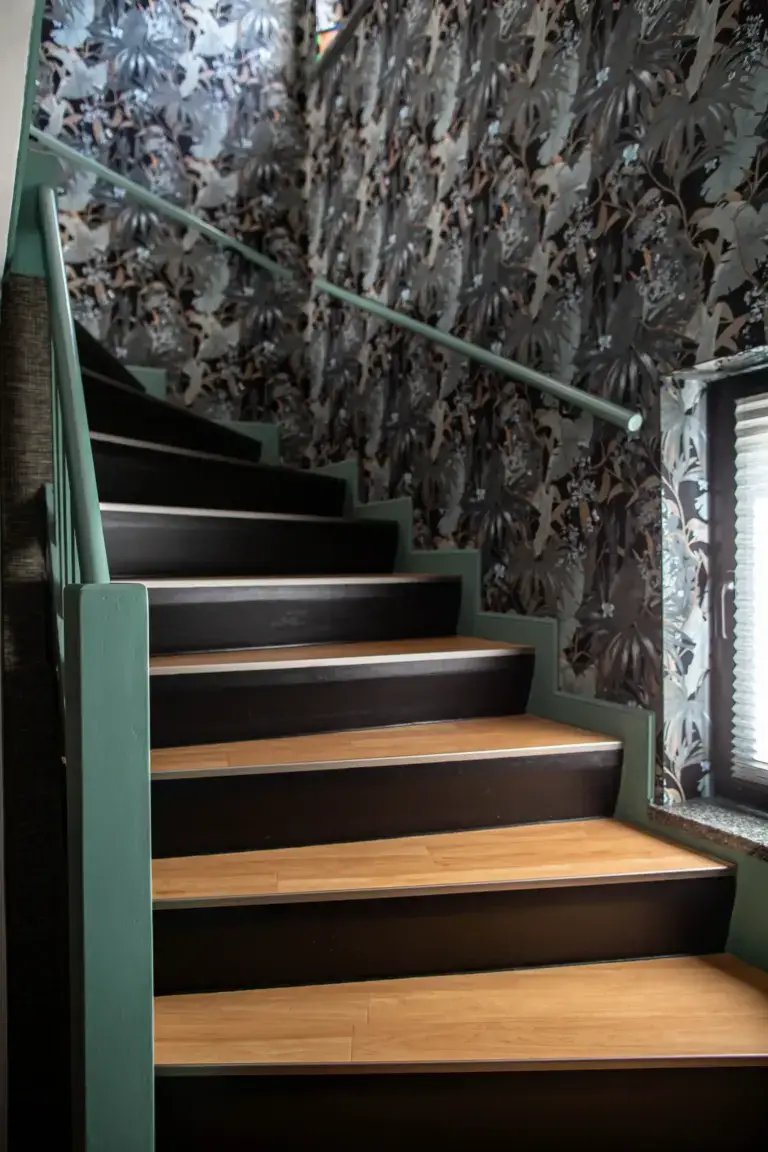 Modern renoviertes Treppenhaus mit salbeigr&uuml;n lackierten Treppenwangen und Handlauf, dunklen Setzstufen und einer edlen Dschungel-Fototapete.