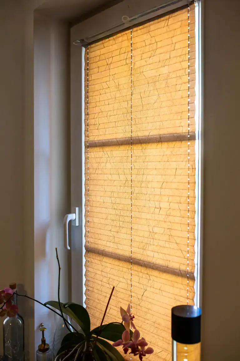 Nahaufnahme eines am Fenster montierten Plissees in warmem Beige mit dekorativer Knitterstruktur als Sicht- und Sonnenschutz.