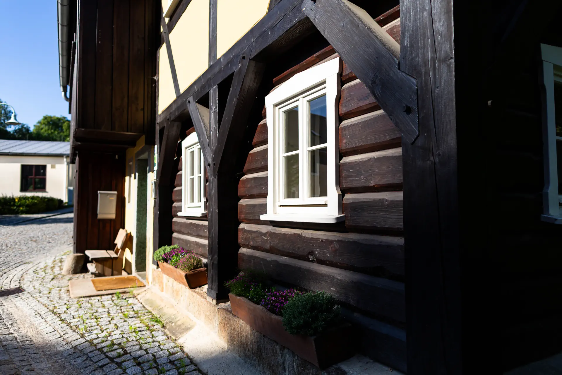 Perspektivische Ansicht der historische Blockbauweise mit massiven Holzbalken und weißen Fensterrahmen.