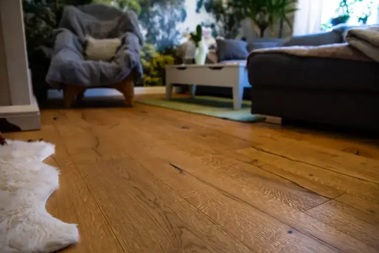 Nahaufnahme der professionellen Bodenverlegearbeiten: Hochwertiger Parkettboden in Wilder Eiche mit markanter Holzmaserung im Wohnzimmer.