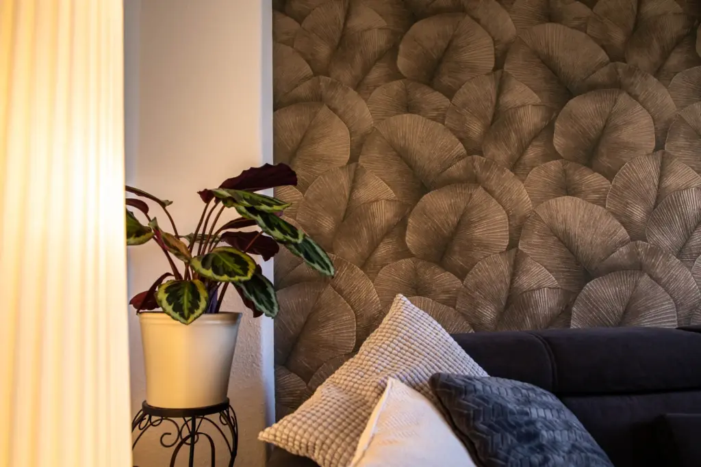 Detailansicht einer Zimmerpflanze im weißen Topf vor der neu gestalteten Wohnzimmerwand mit eleganter Mustertapete.