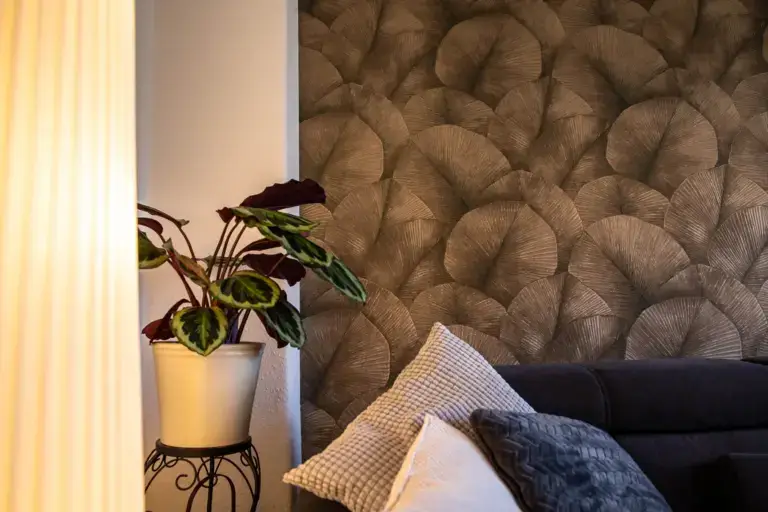 Detailansicht einer Zimmerpflanze im weißen Topf vor der neu gestalteten Wohnzimmerwand mit eleganter Mustertapete.