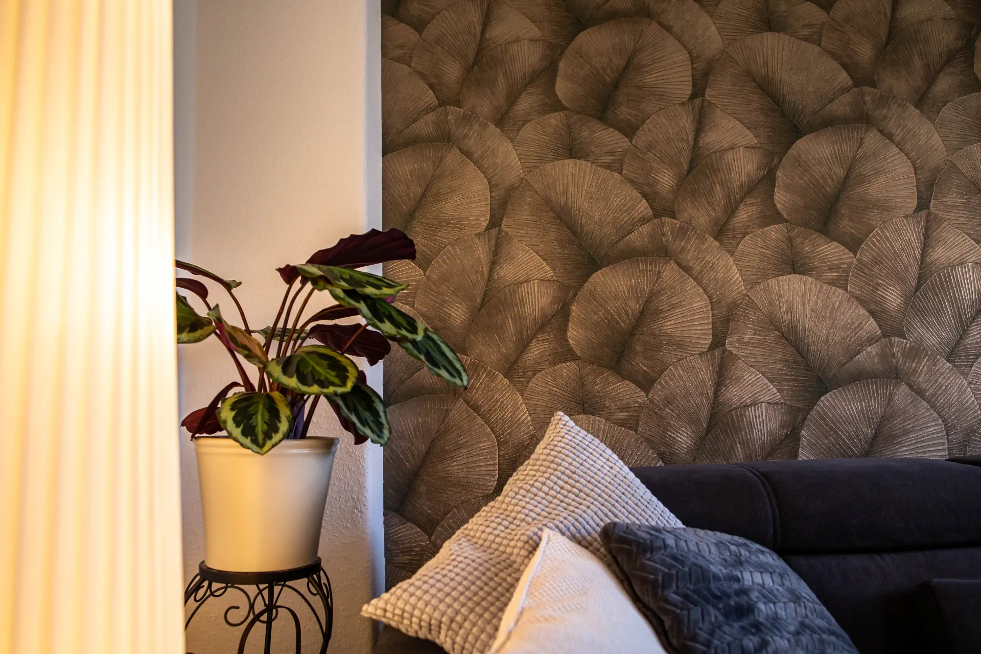 Detailansicht einer Zimmerpflanze im weißen Topf vor der neu gestalteten Wohnzimmerwand mit eleganter Mustertapete.