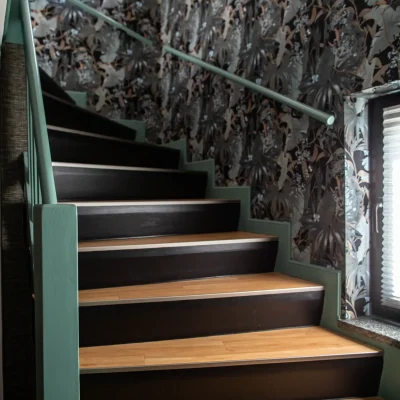 Modern renoviertes Treppenhaus mit salbeigrün lackierten Treppenwangen und Handlauf, dunklen Setzstufen und einer edlen Dschungel-Fototapete.