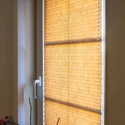 Nahaufnahme eines am Fenster montierten Plissees in warmem Beige mit dekorativer Knitterstruktur als Sicht- und Sonnenschutz.