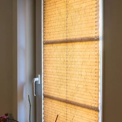 Nahaufnahme eines am Fenster montierten Plissees in warmem Beige mit dekorativer Knitterstruktur als Sicht- und Sonnenschutz.