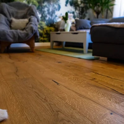 Nahaufnahme der professionellen Bodenverlegearbeiten: Hochwertiger Parkettboden in Wilder Eiche mit markanter Holzmaserung im Wohnzimmer.