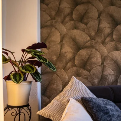 Detailansicht einer Zimmerpflanze im weißen Topf vor der neu gestalteten Wohnzimmerwand mit eleganter Mustertapete.