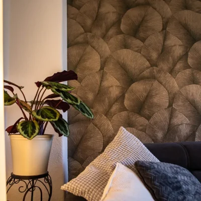 Detailansicht einer Zimmerpflanze im weißen Topf vor der neu gestalteten Wohnzimmerwand mit eleganter Mustertapete.